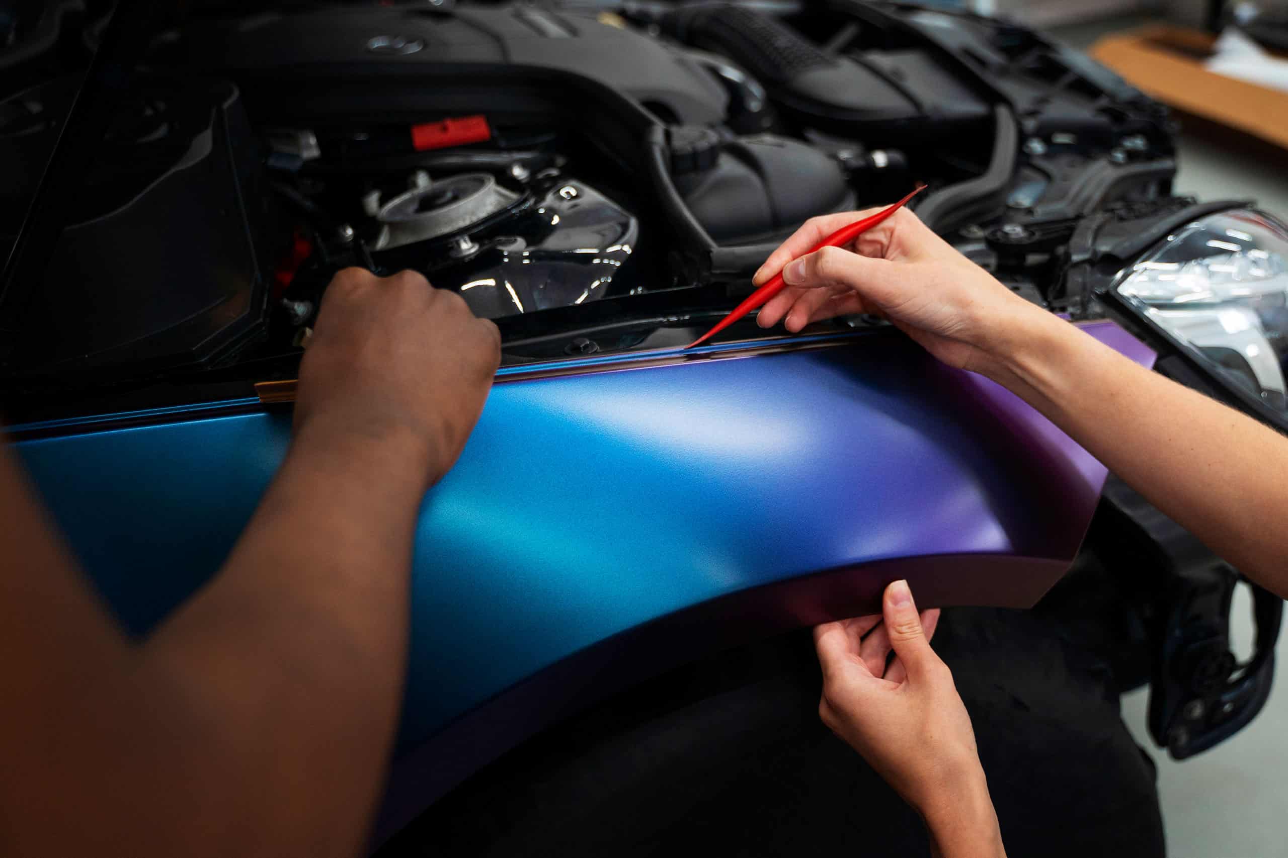 Detailarbeit bei der Fahrzeugfolierung: blau-violette Folie wird an einer Karosseriekante angelegt